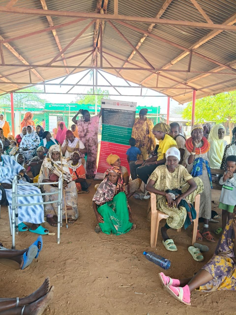 FAN banner visible at a community meeting with elderly women present