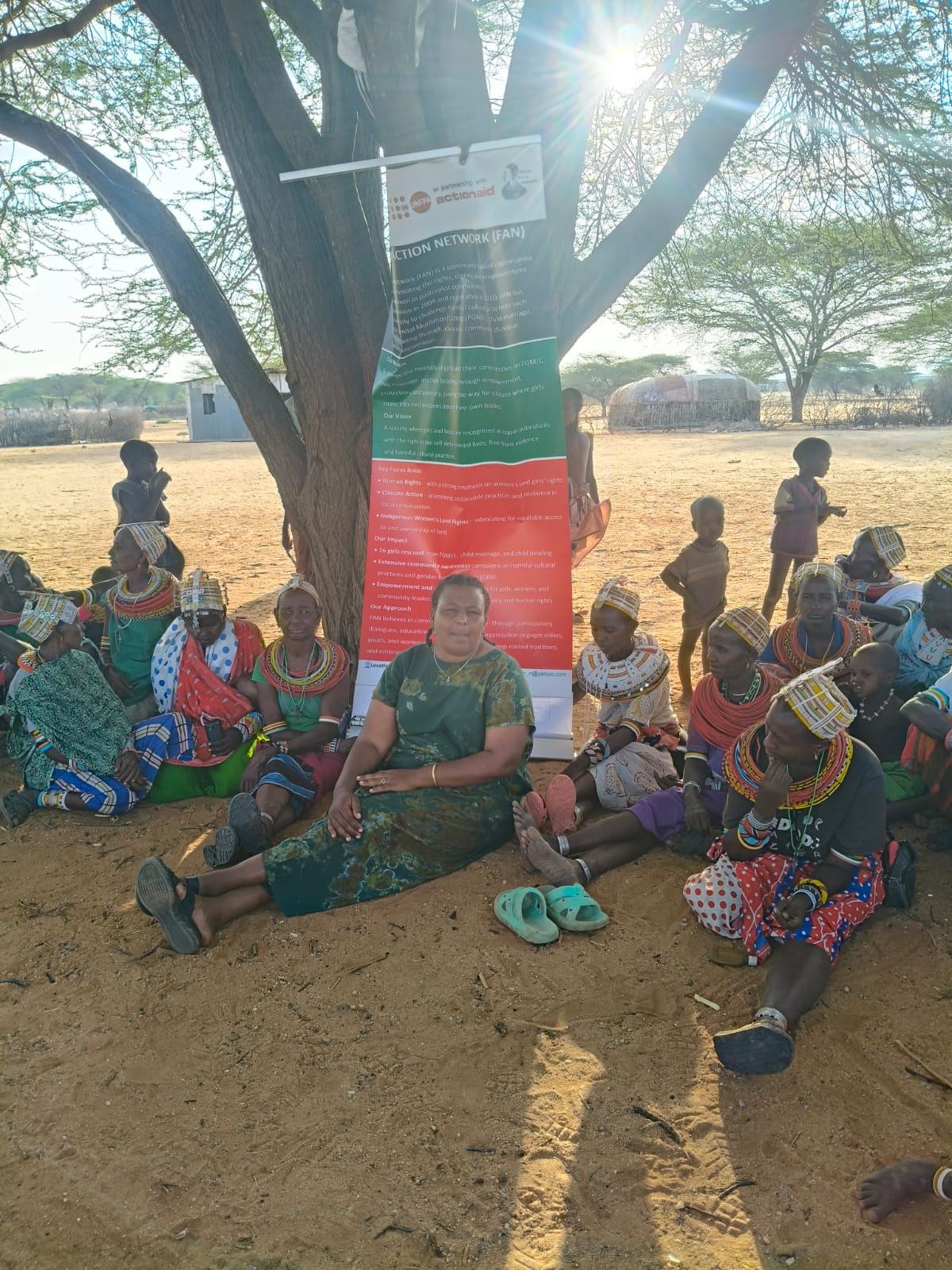 Samburu and Rendille women gathered under a tree in Laisamis holding the Feiyah Action Network banner